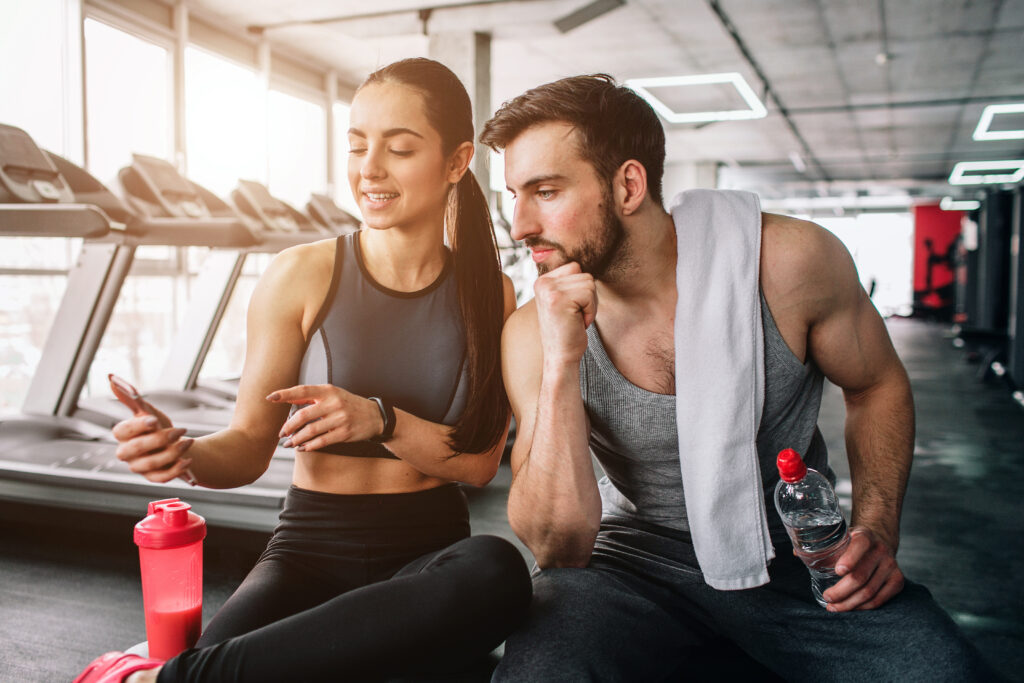 Close up of a girl sitting on the sport bench and showing something on the phone to her sport partner