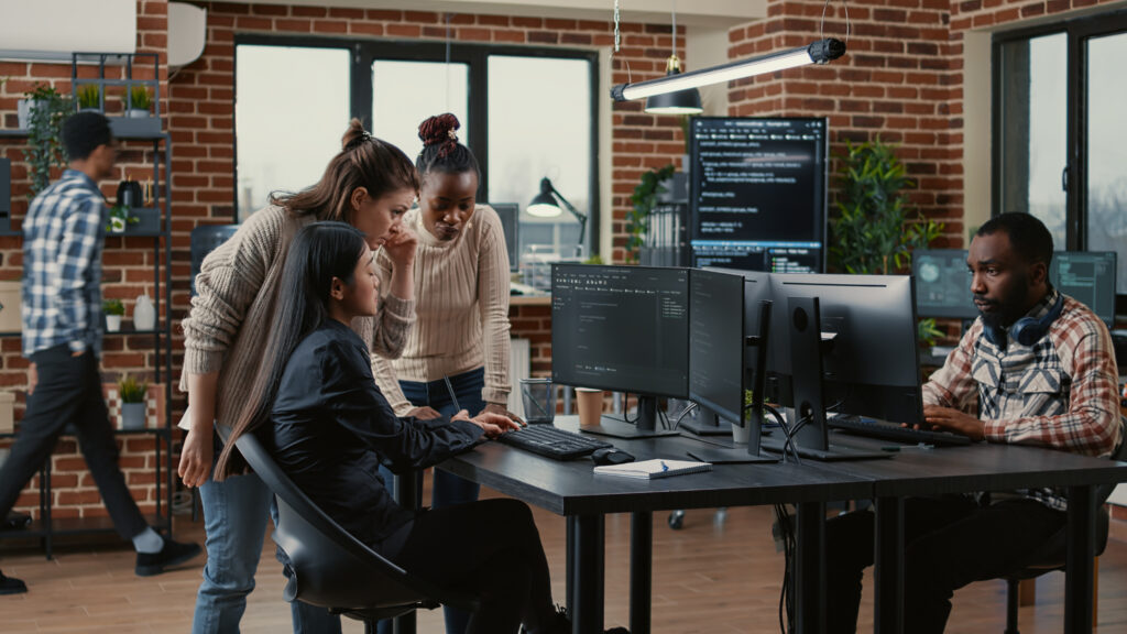 Team of software engineers brainstorming ideas for new code library in front of computer screens compiling algorithms.