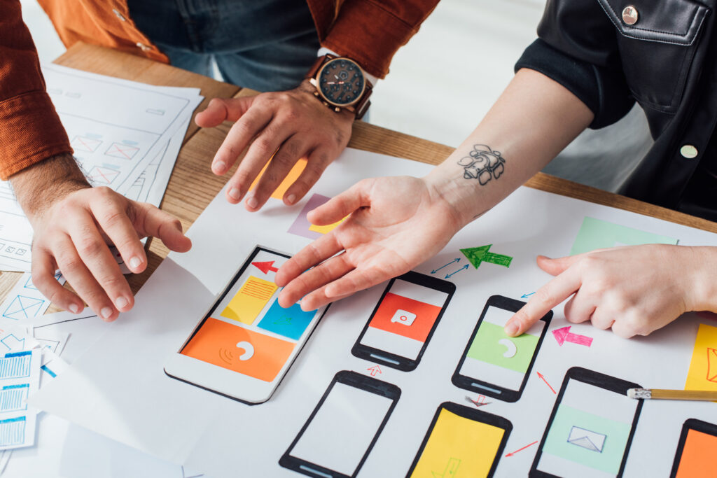 Cropped view of ux designers working with sketches and mobile wireframe layouts at table