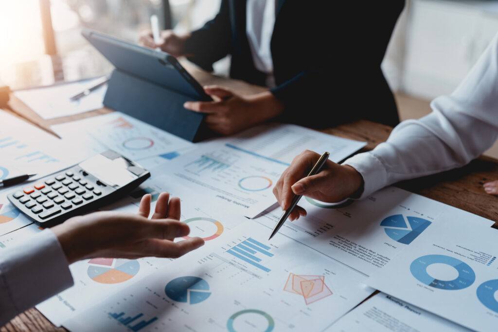 Image of a group of business people meeting using a tablet and calculating calculator to plan, analyze, graph and chart their organization's growth to plan future business expansion.