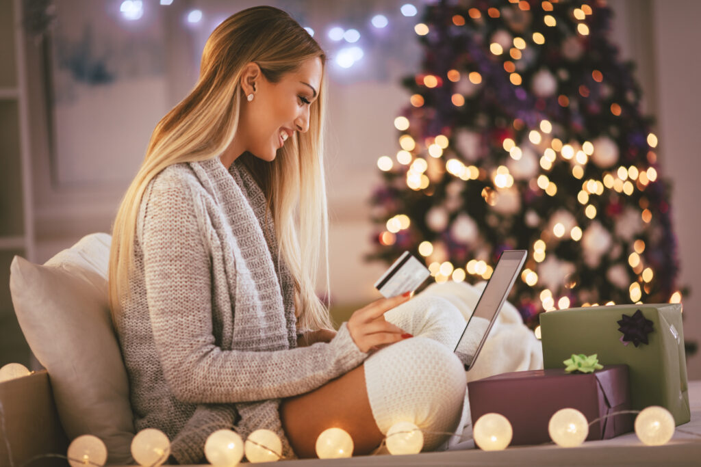 Happy young woman relaxing at home and online buying Christmas presents on laptop.